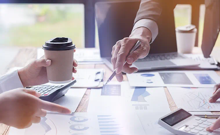Two business people looking over reports across a desk in an office.