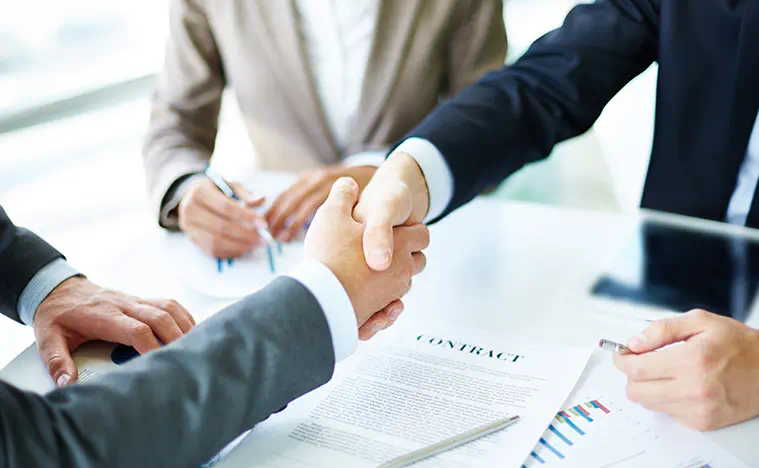 Two business men shake hands at a conference table.