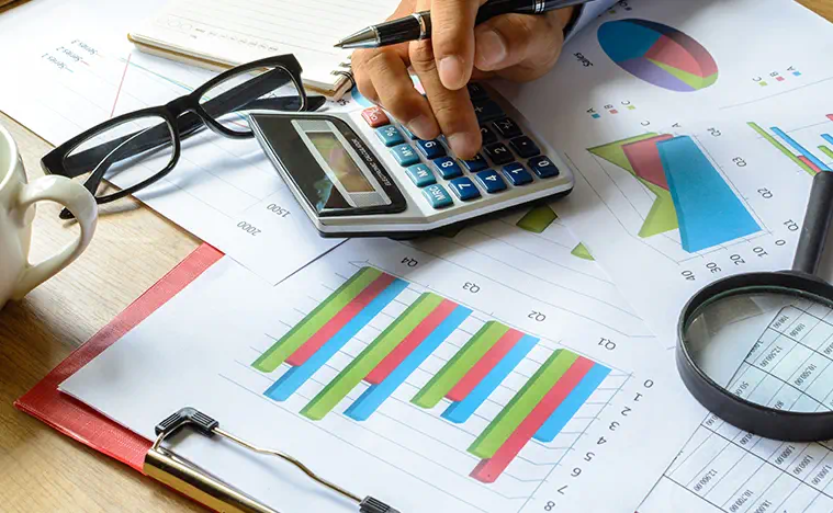 Close up of someone looking over reports and using a calculator.